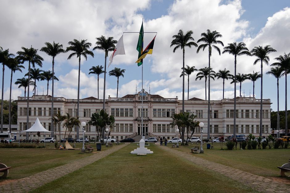 Política Nacional — Elegant municipal building in Juiz de Fora, Brazil, surrounded by palm trees under a cloudy sky.